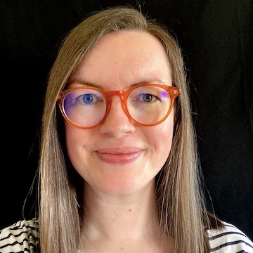 Head photo of Hannah Ross, who is smiling at the camera. The background is very dark. She has light brown hair and orange glasses.